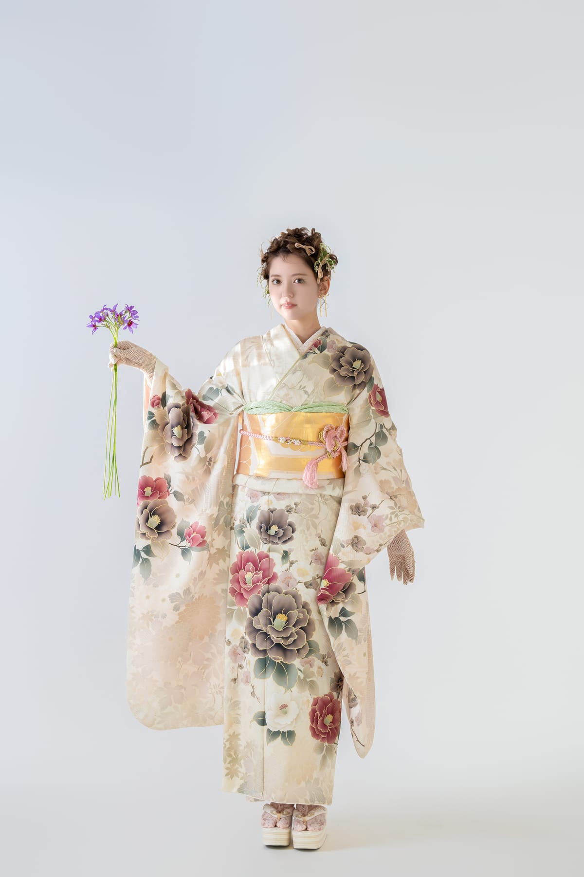 生成り地に花柄の振袖。白い背景で花を掲げた全身