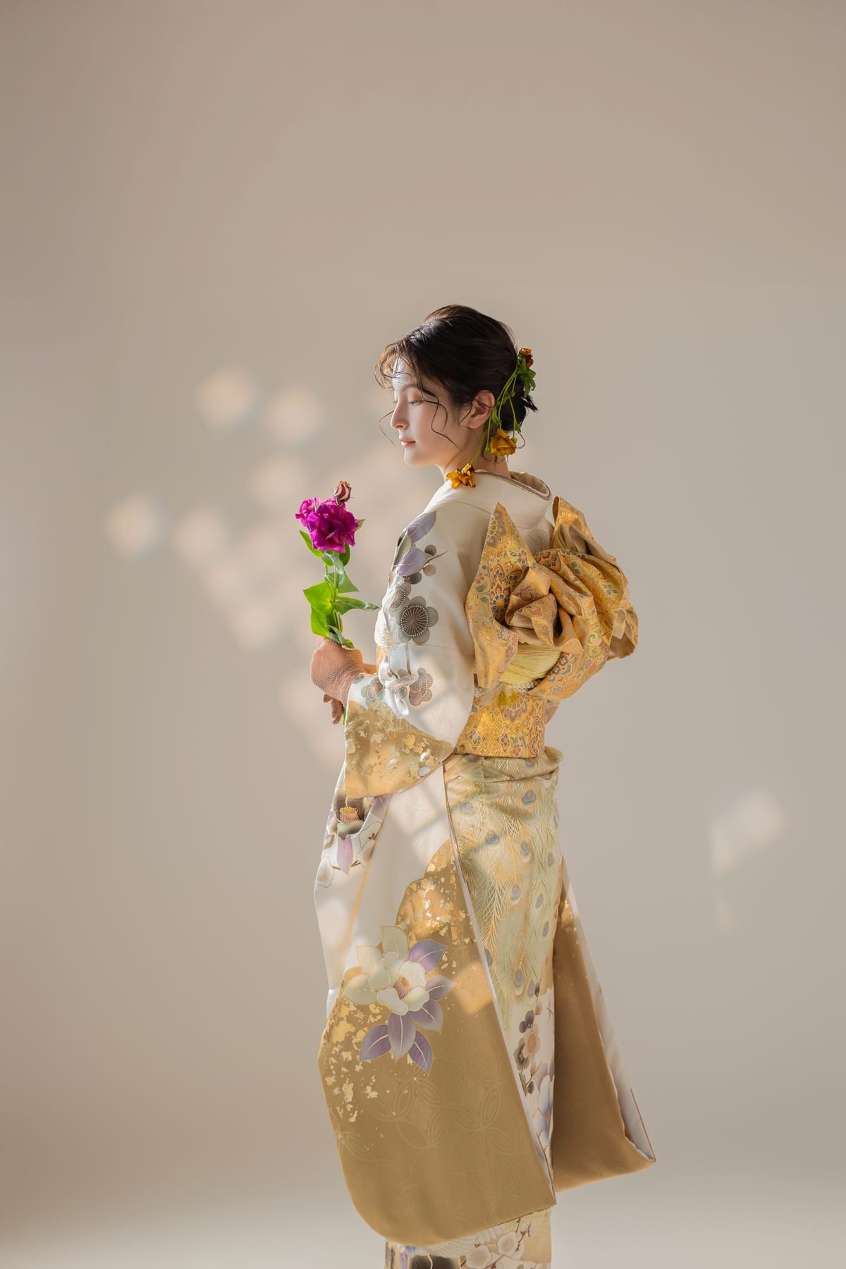 金と生成りの振袖。濃いピンクの花を持った姿です。成人式の前撮り写真