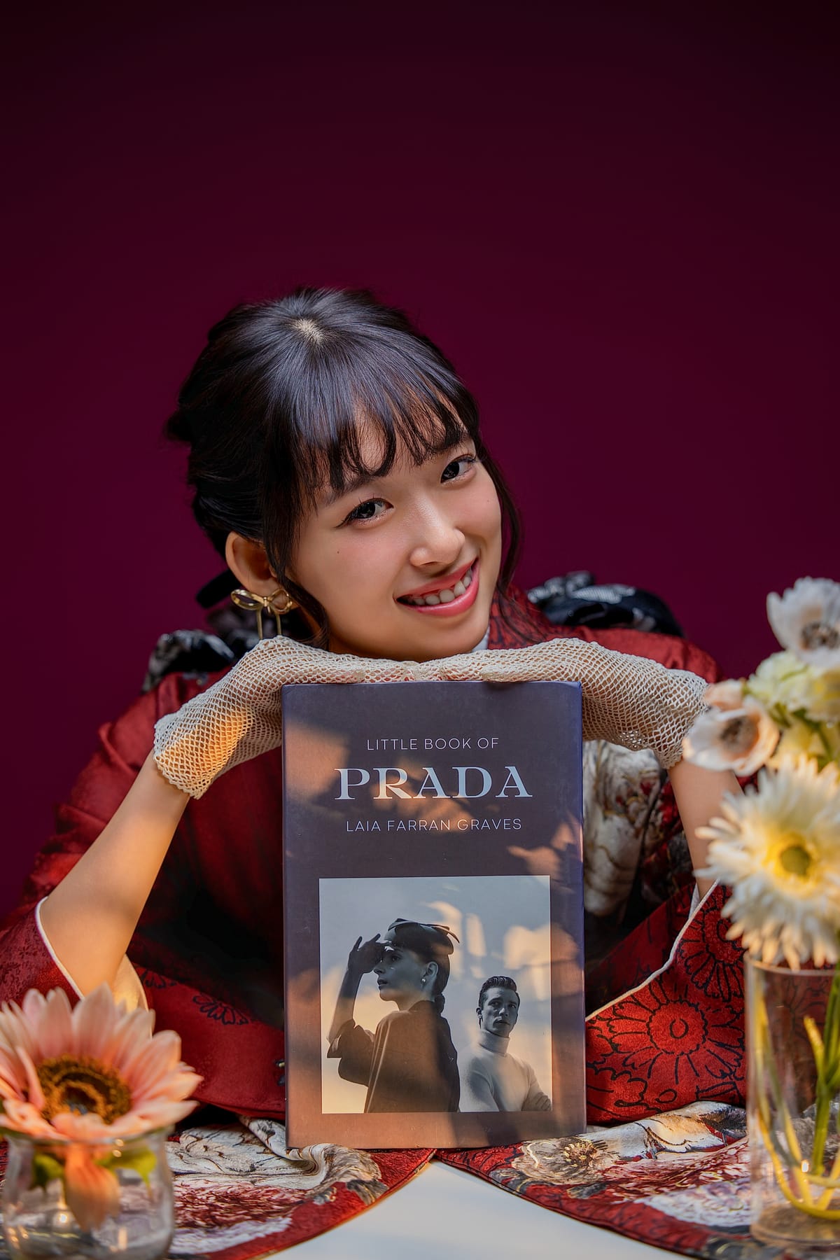 赤い振袖。臙脂の背景で洋書と花を置いたテーブルに着く姿