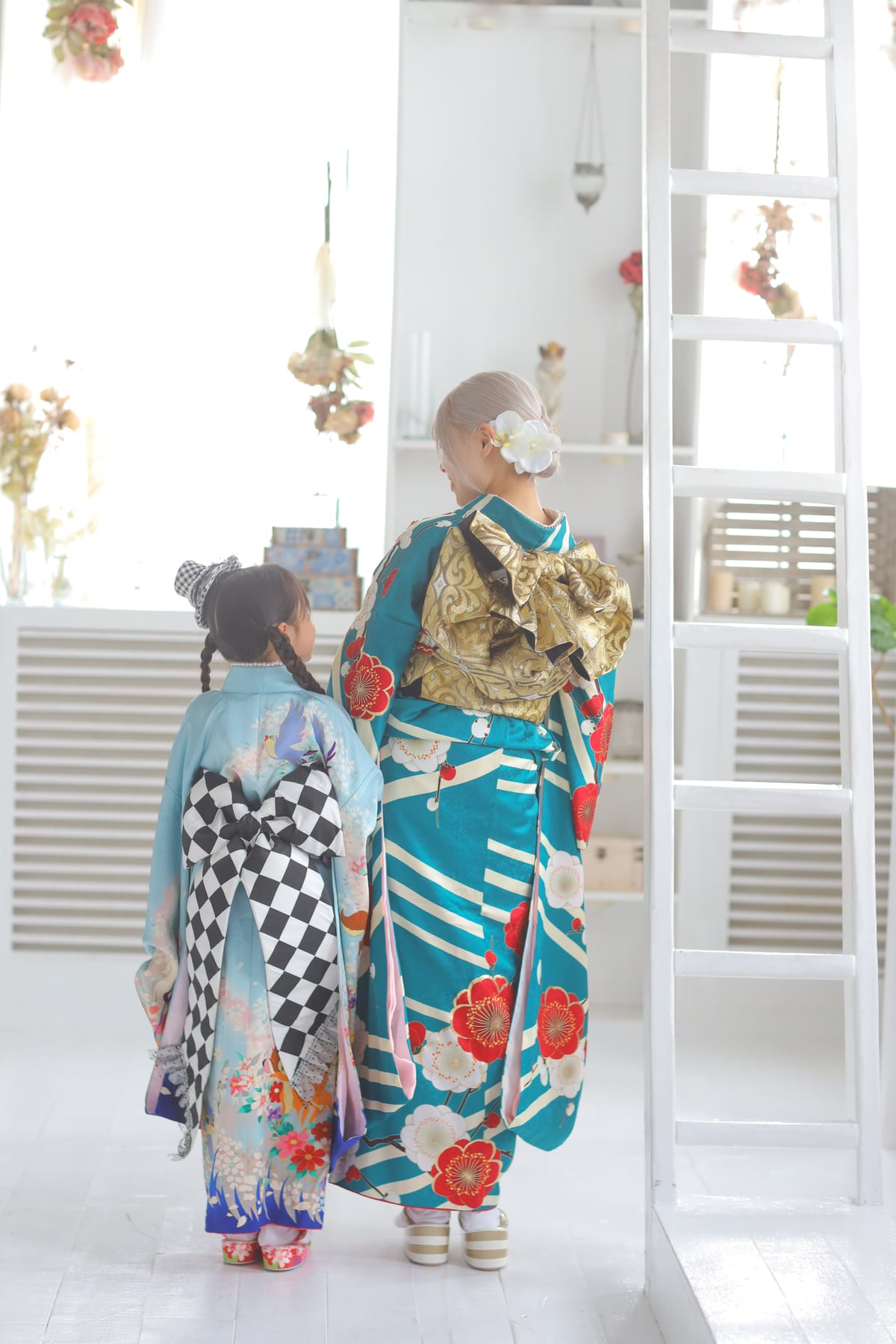 ターコイズの振袖の女性と着物姿の子どもの後ろ姿です。成人式の前撮り写真