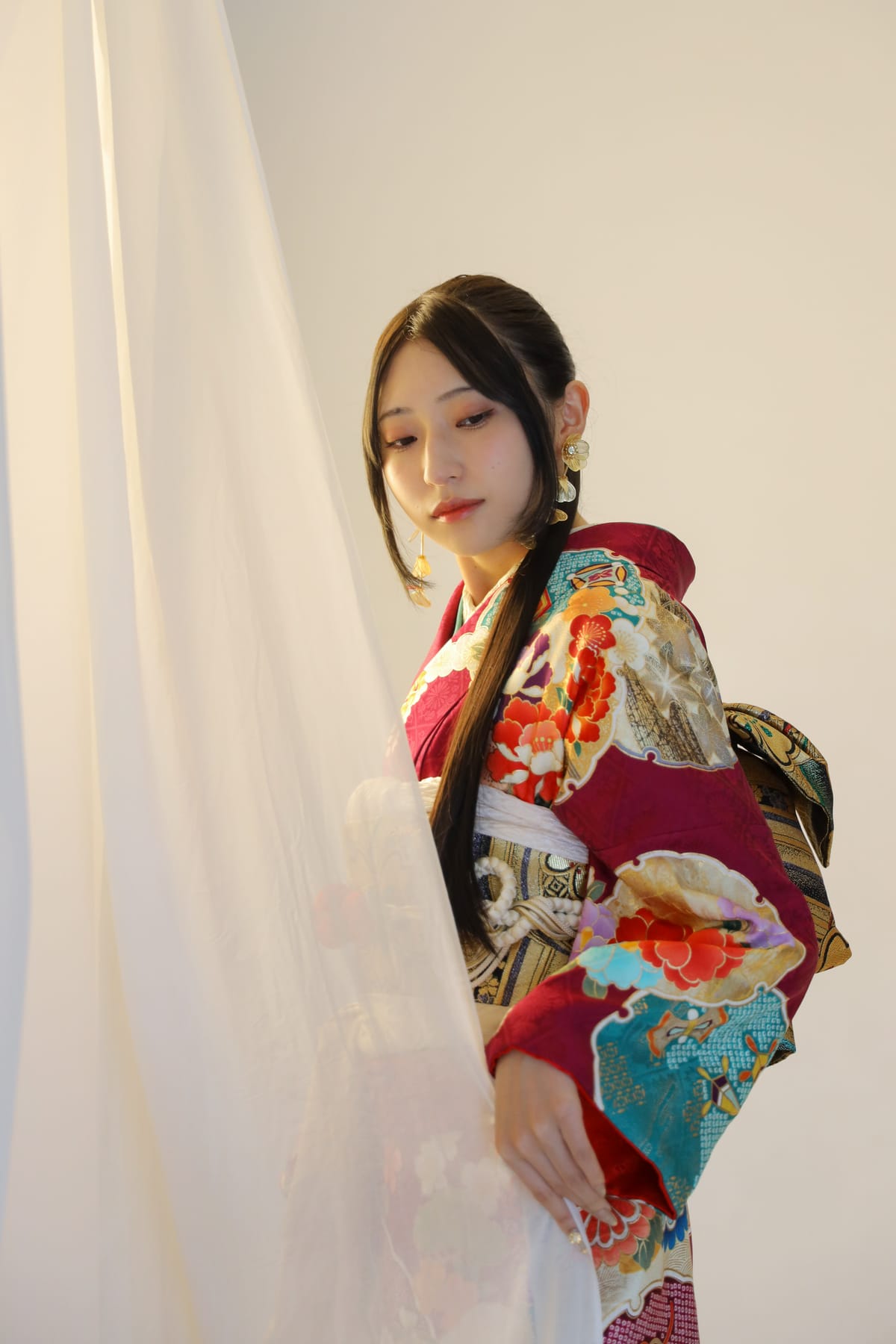 深紅にターコイズの振袖。カーテン越しの光の中に立つ姿