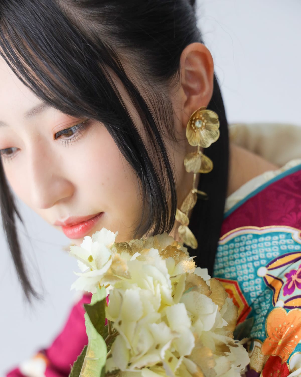 深紅にターコイズの振袖。白い花を肩に寄せた横顔の寄りです。成人式の前撮り写真