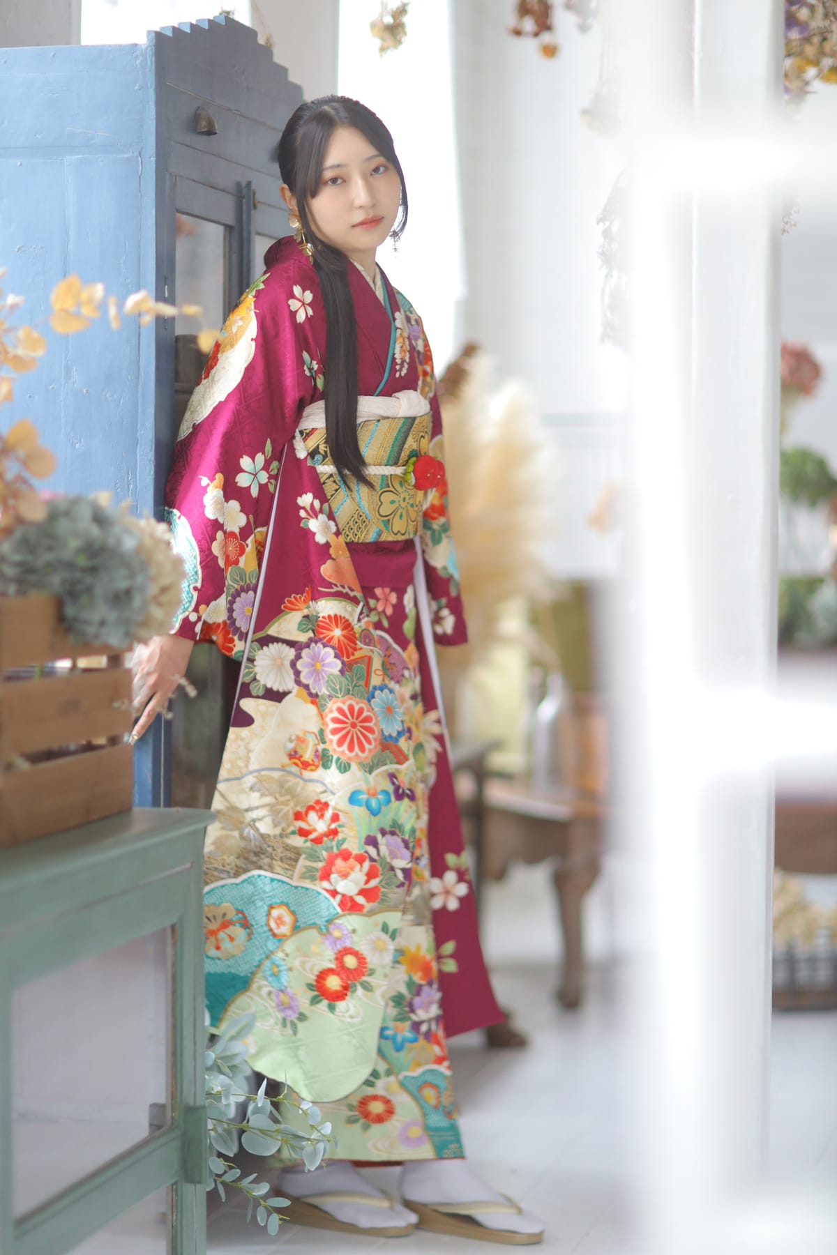 青みを含んだ深紅の振袖。青い扉の前に立つ姿