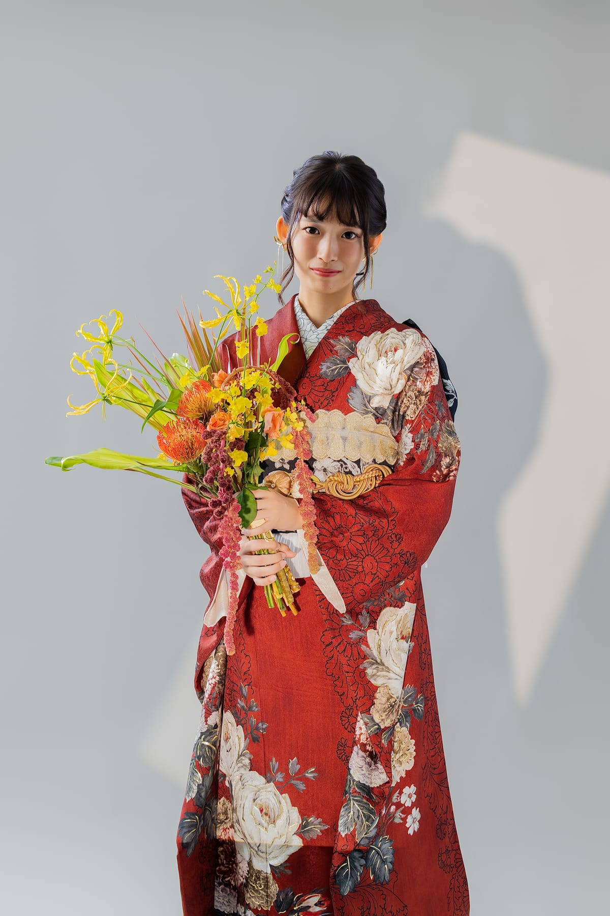 明るい赤の振袖。白い牡丹柄。白い背景で花束を抱えた全身