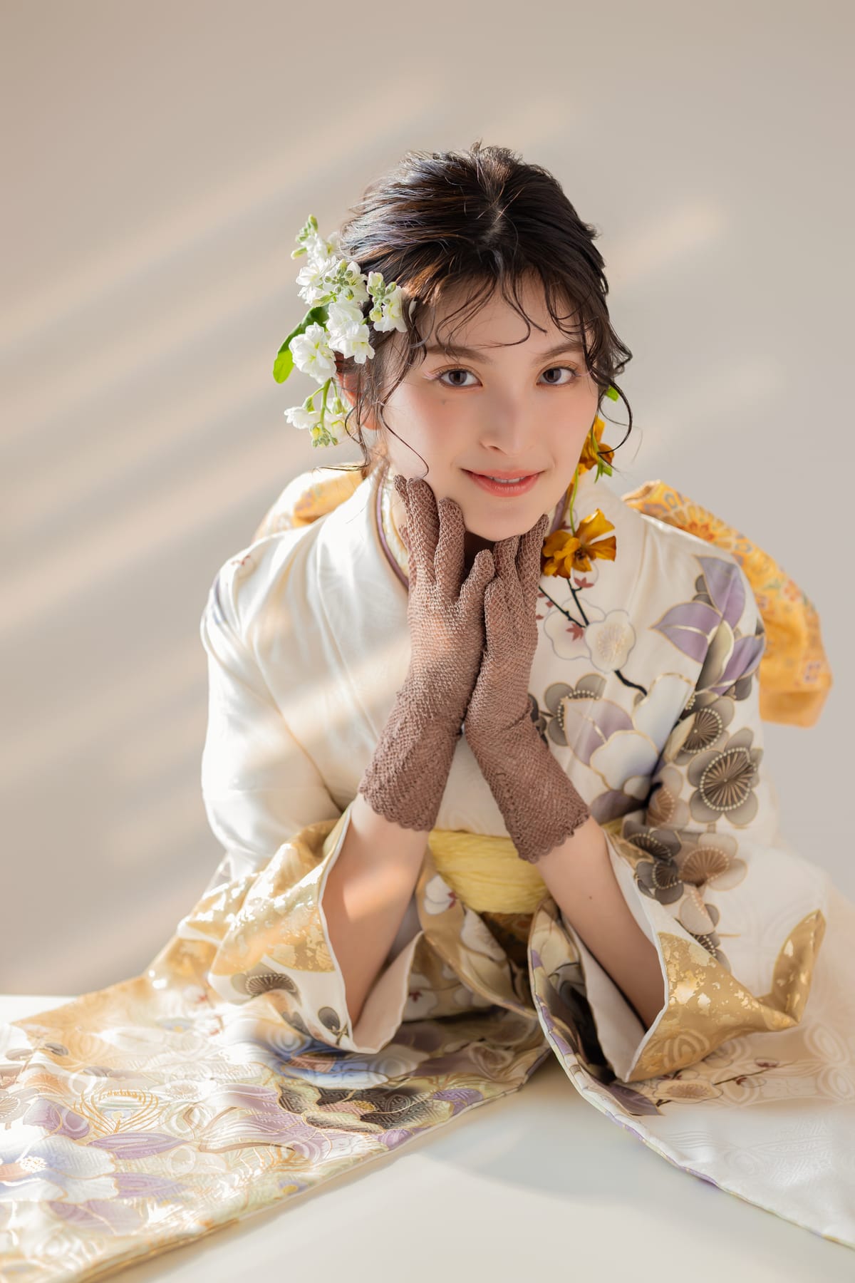 白と金の淡い花柄の振袖。頬に手を添えた寄りの写真