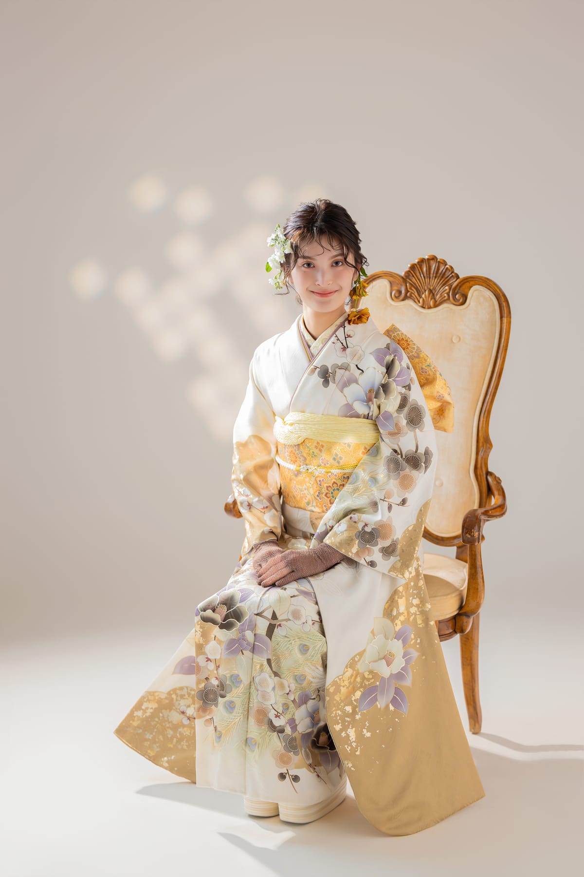 白と金の淡い花柄のシンプルな振袖。椅子に腰かけた姿