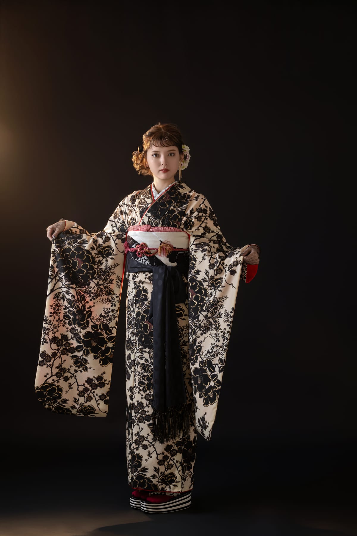生成りに黒い花の振袖。両袖を広げて立つ全身