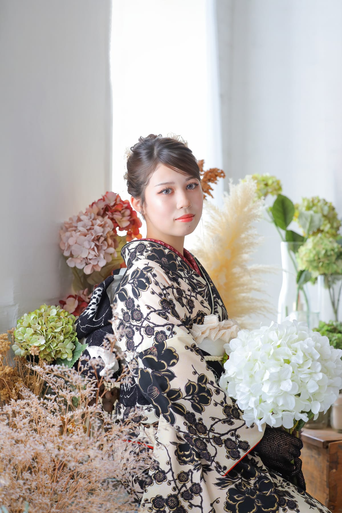 生成りに黒い花の振袖。ドライフラワーに囲まれて座る姿