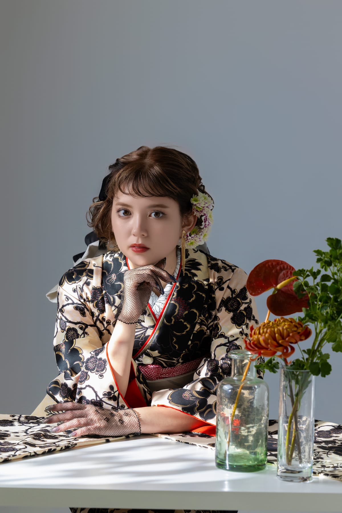 生成りに黒い花の振袖。机の花に手を添えて座る上半身