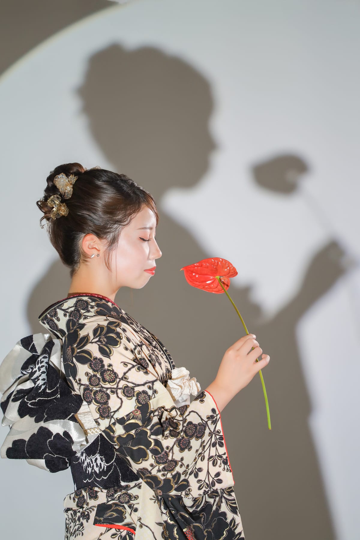 生成りに黒い花の振袖。赤い花に顔を寄せた横顔