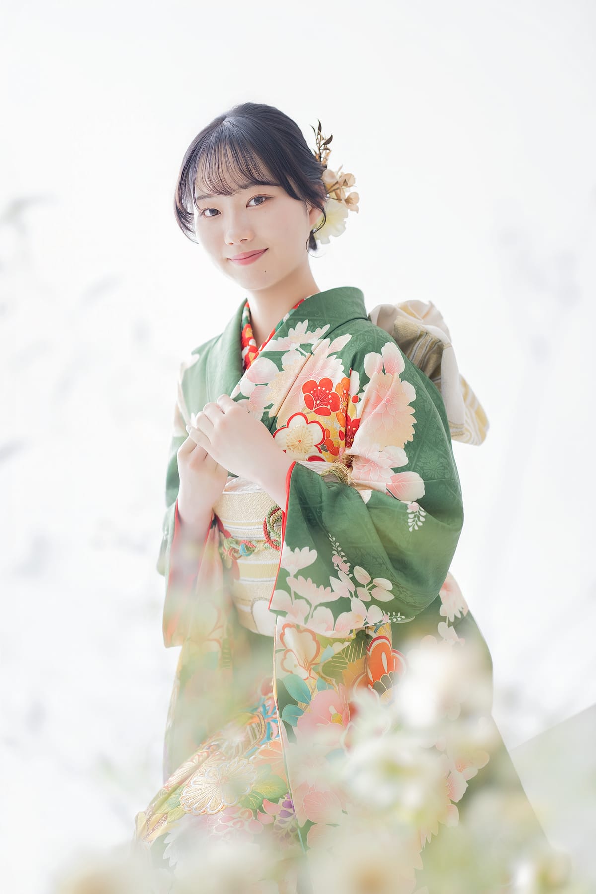 緑地に花の振袖。髪飾りをつけたまとめ髪の上半身