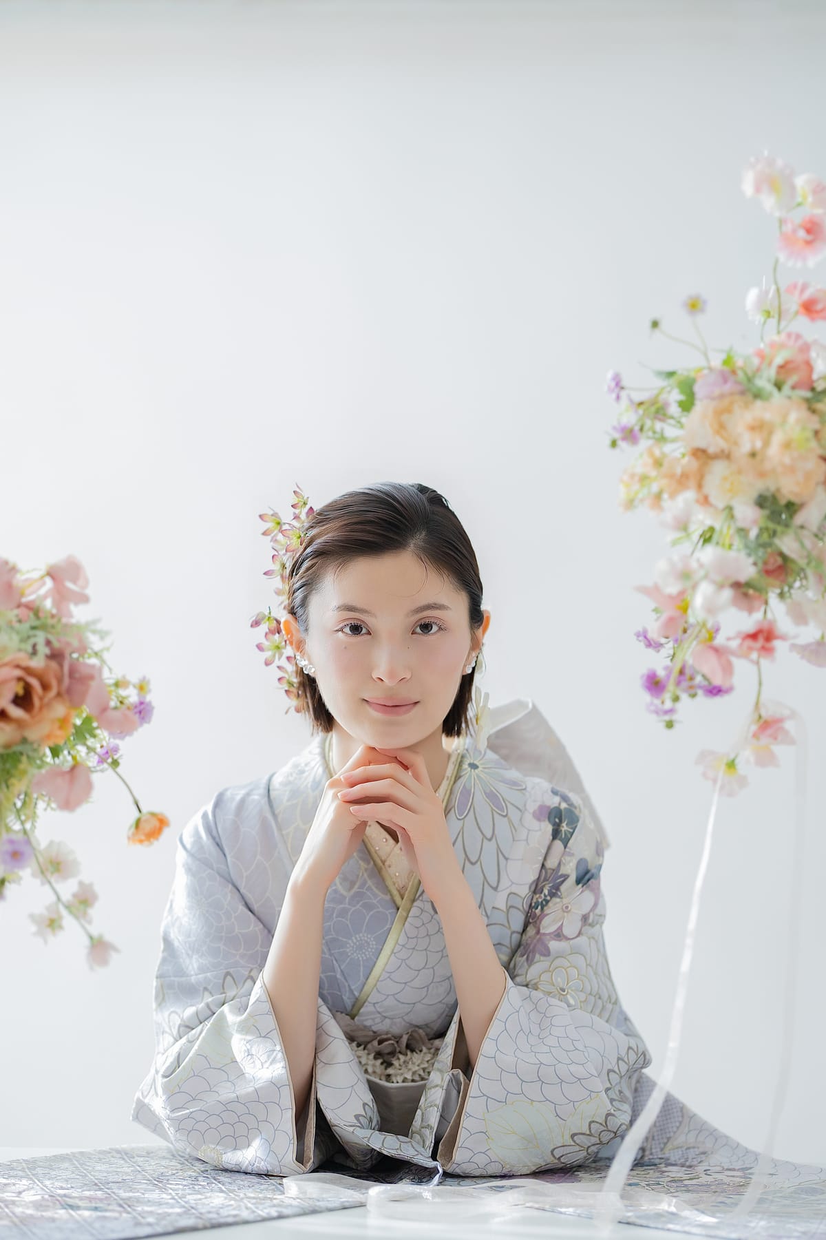 銀鼠の振袖。花に囲まれ、手を組んで座る上半身