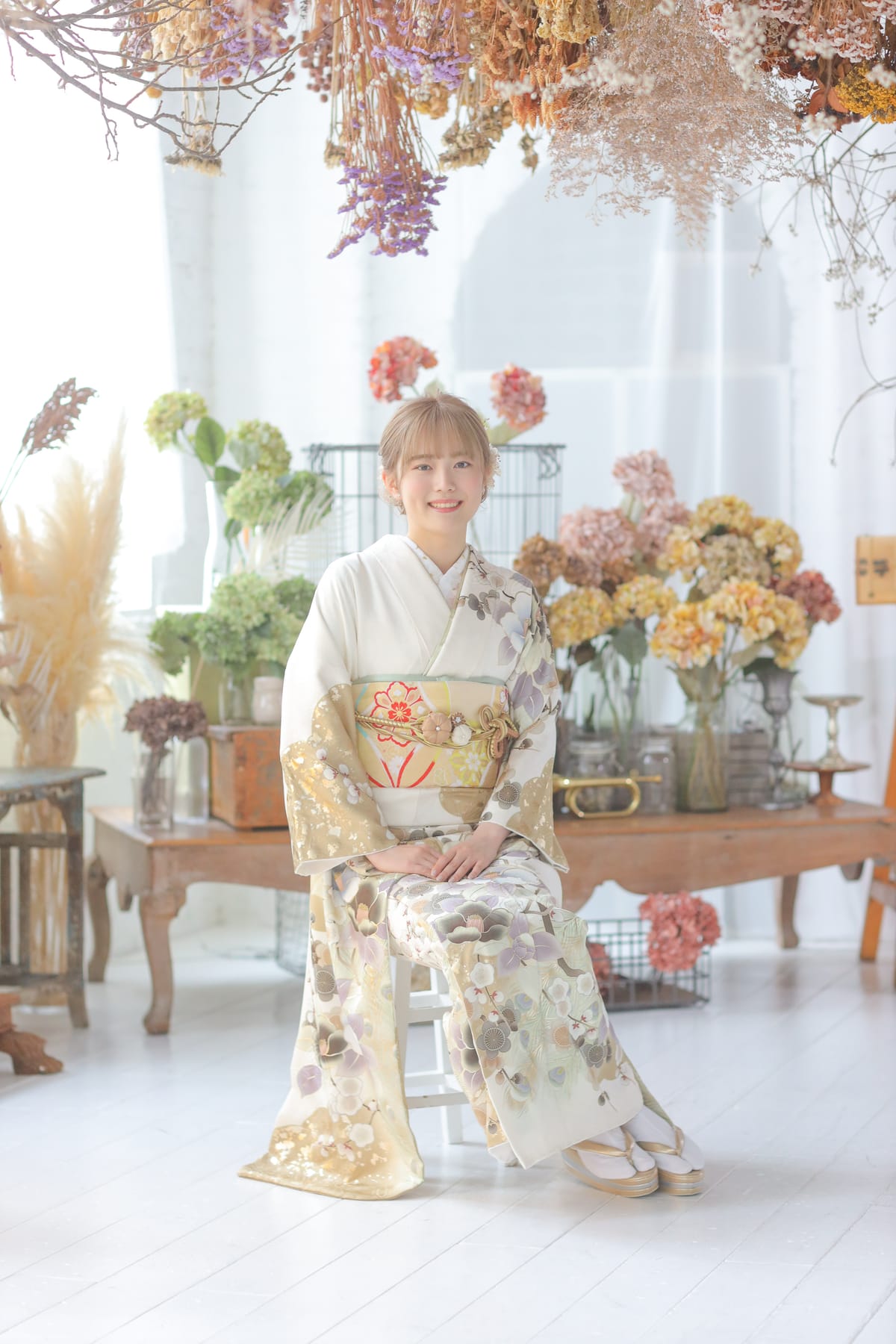 白地に花の振袖。花のある空間で椅子に座る全身