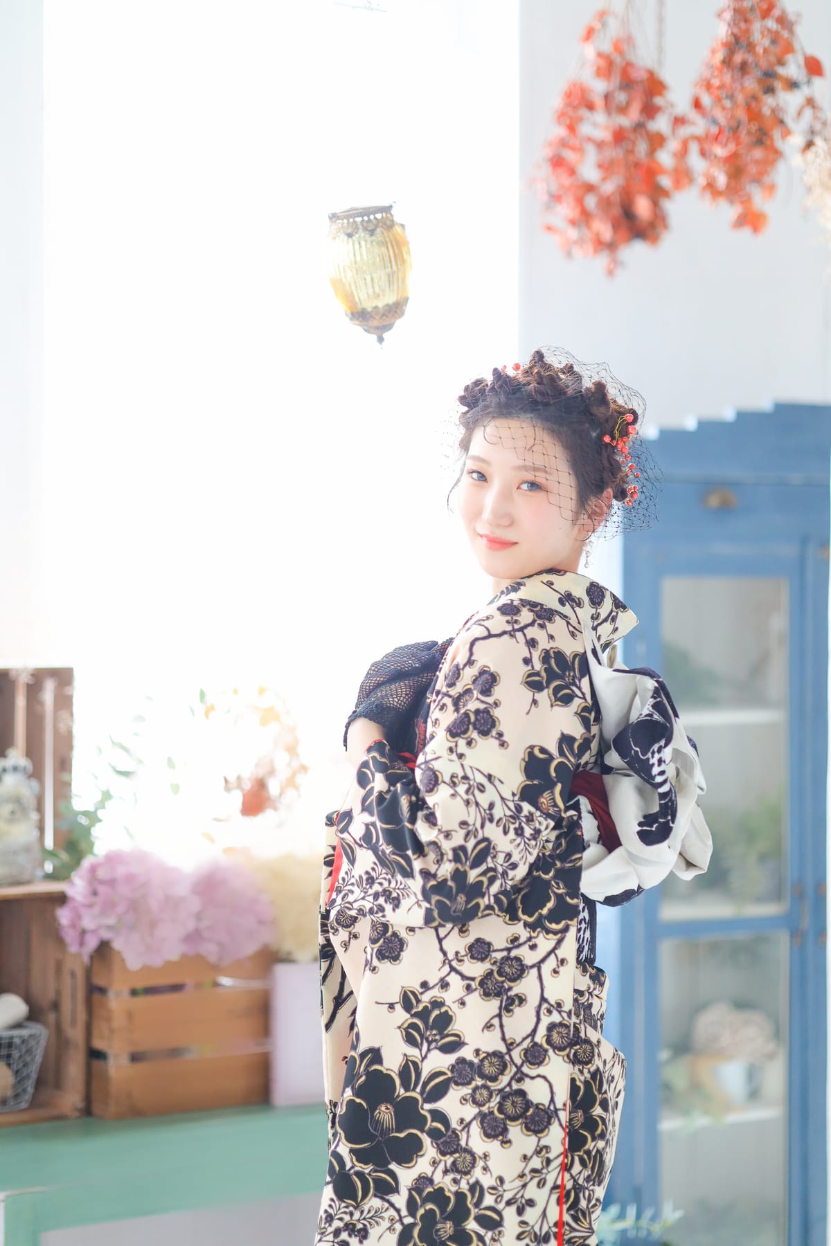 生成りに黒い花の振袖。青い扉のある明るい空間で振り返る姿