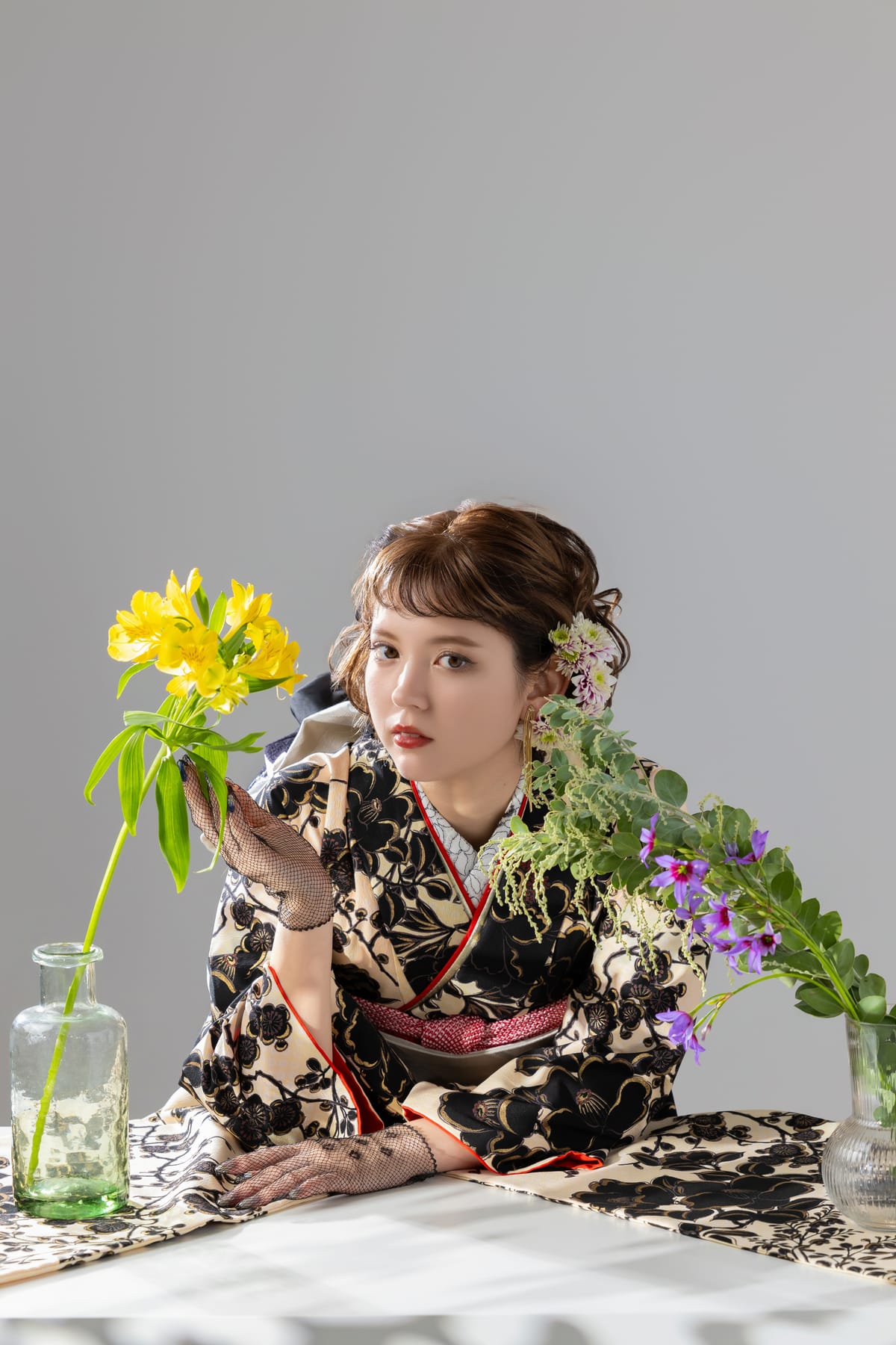 黒地に花の振袖。机の花に手を添えた上半身