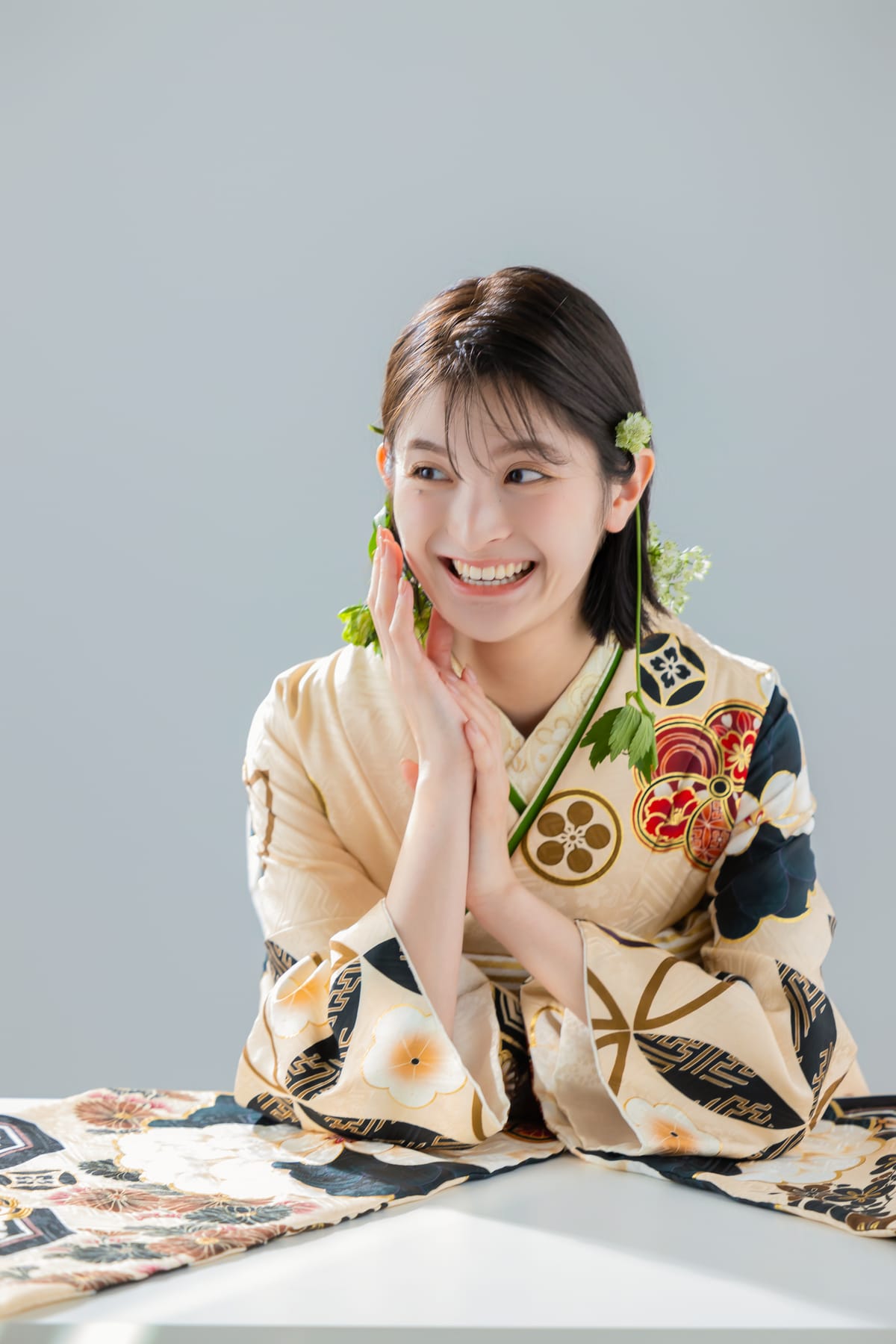 生成りに古典柄の振袖。机に手を重ねて笑う上半身