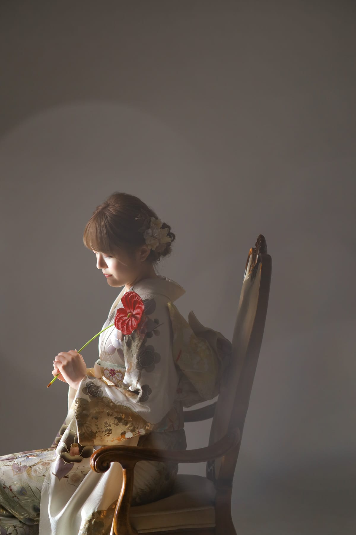 白地に花の振袖。椅子に横向きに座り目線を落とした姿