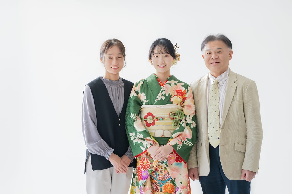 緑の振袖の女性を中心に、私服のご家族2名が並んだ写真