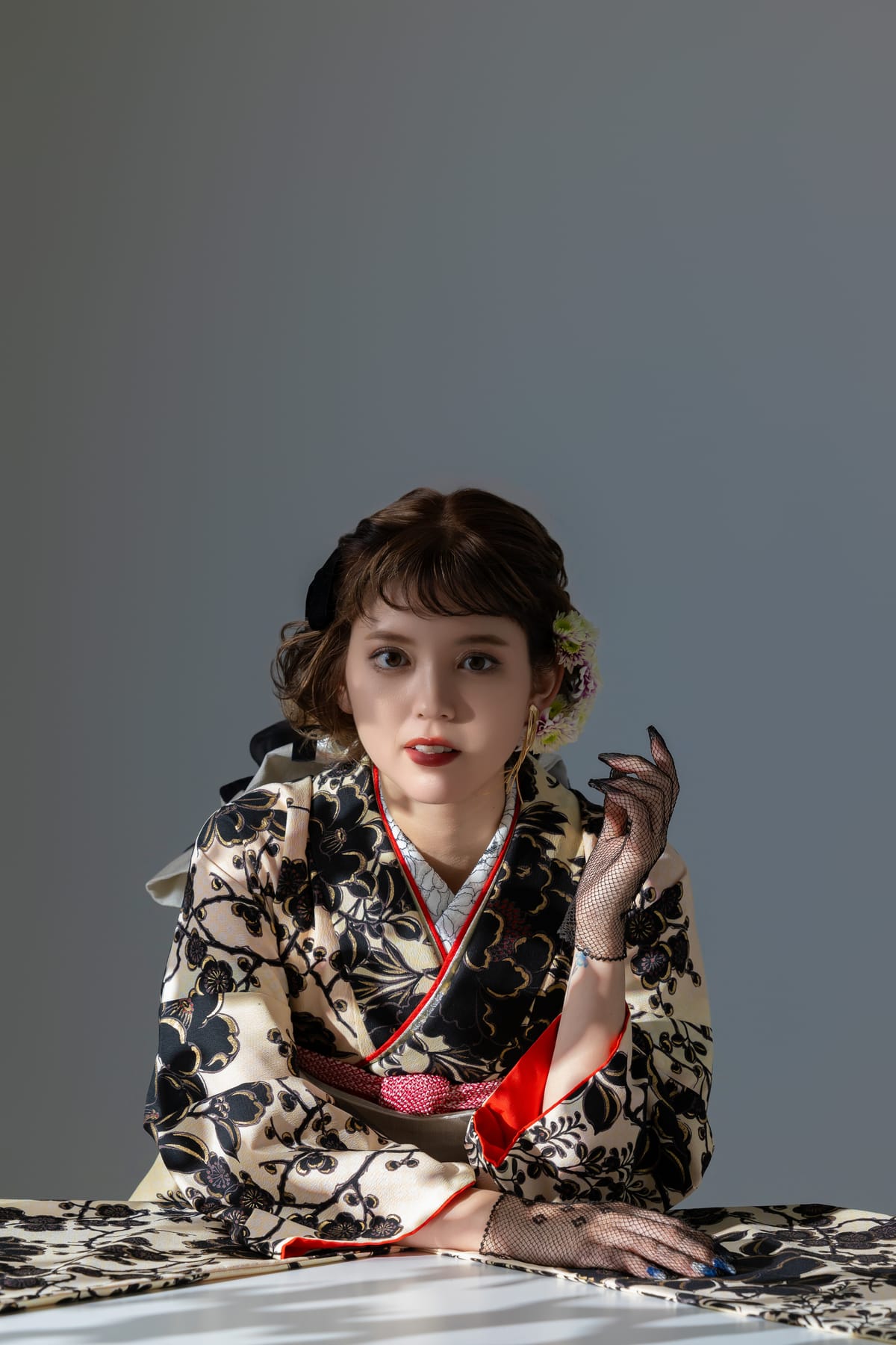 生成りに黒い花の振袖。机に手を置いて正面を見る上半身