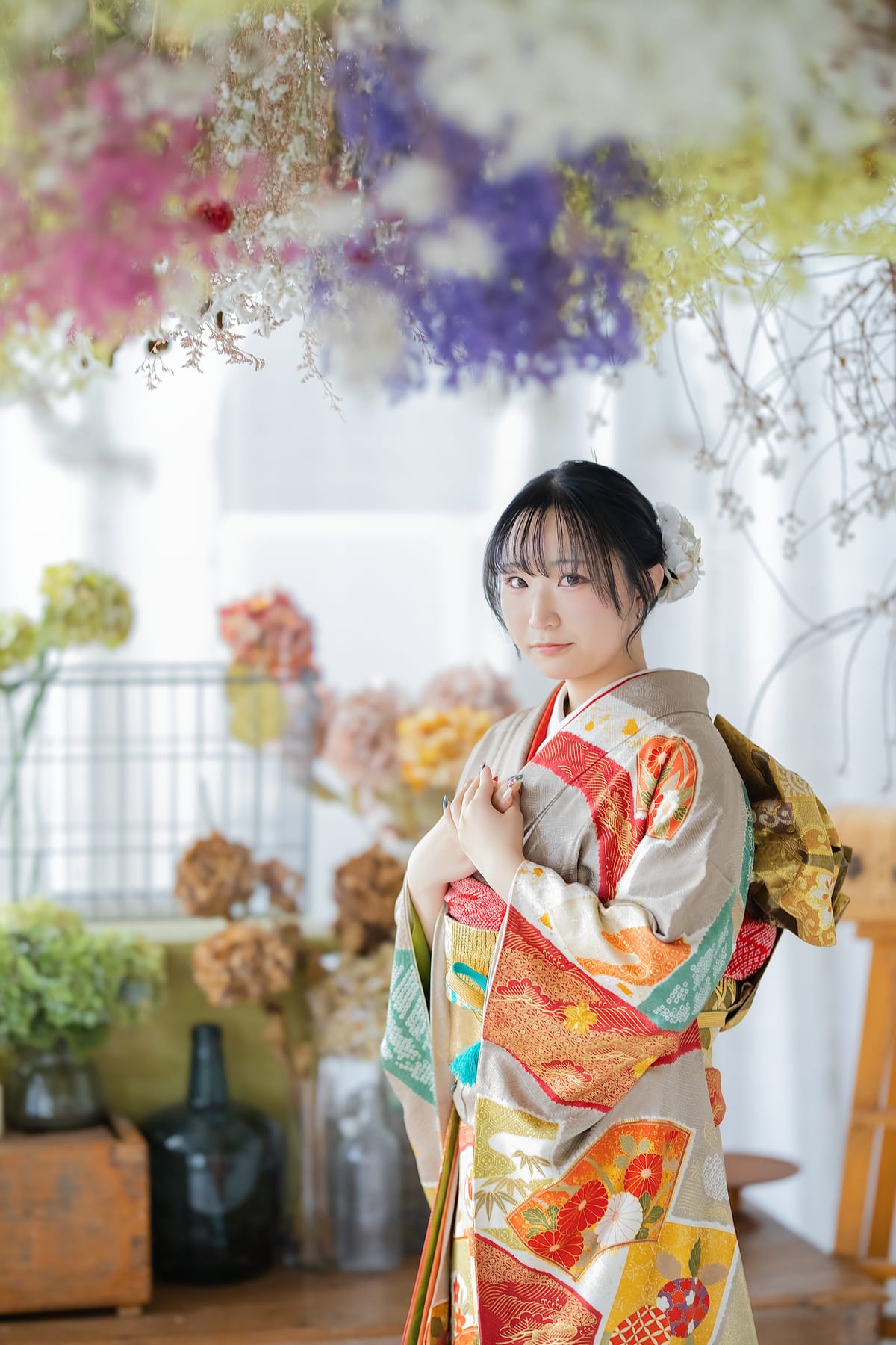 生成りに彩り豊かな柄の振袖。花に囲まれて袖を抱えた上半身
